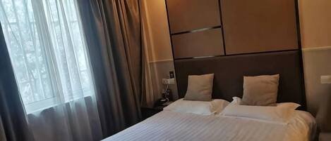 Habitación de hotel con una cama grande, una mesita de noche y un ventanal con cortinas.
