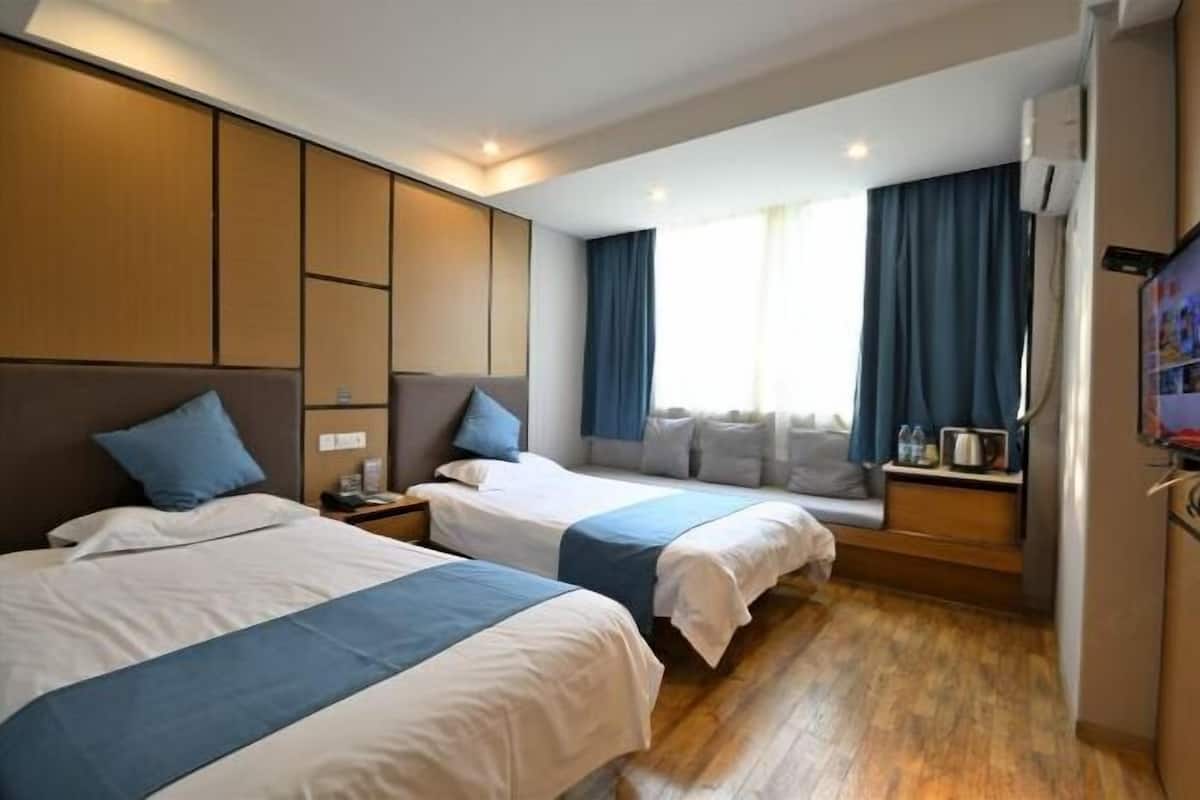Ein Hotelzimmer mit zwei Betten, einer Sitzecke, einem Fernseher und einem Fenster mit Vorhängen.