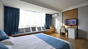 A modern hotel room with a large bed, a desk, a chair, a television, and a window with curtains.