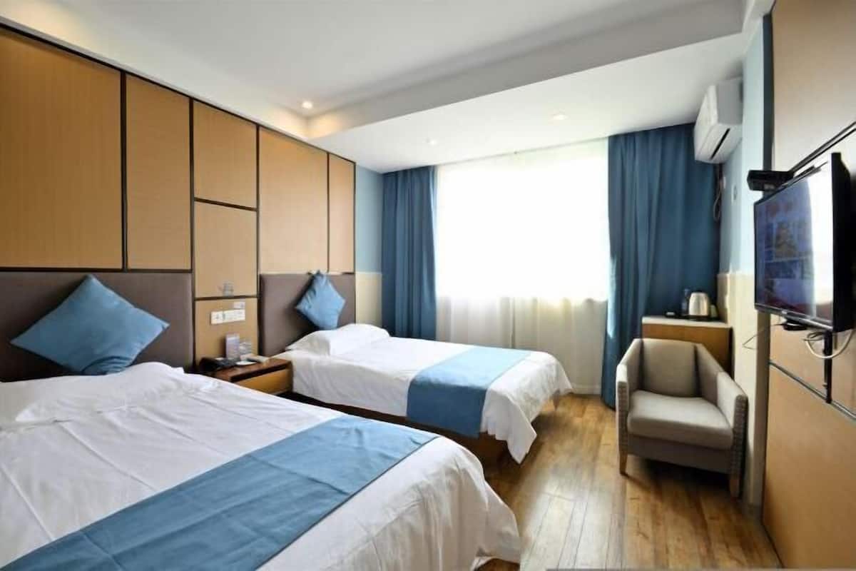 Ein Hotelzimmer mit zwei Betten, einem Fernseher, einem Sessel und einem Fenster mit Vorhängen.