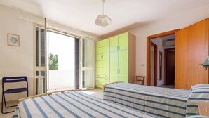 Un dormitorio con dos camas, una silla, un armario y una puerta que da a otra habitación.