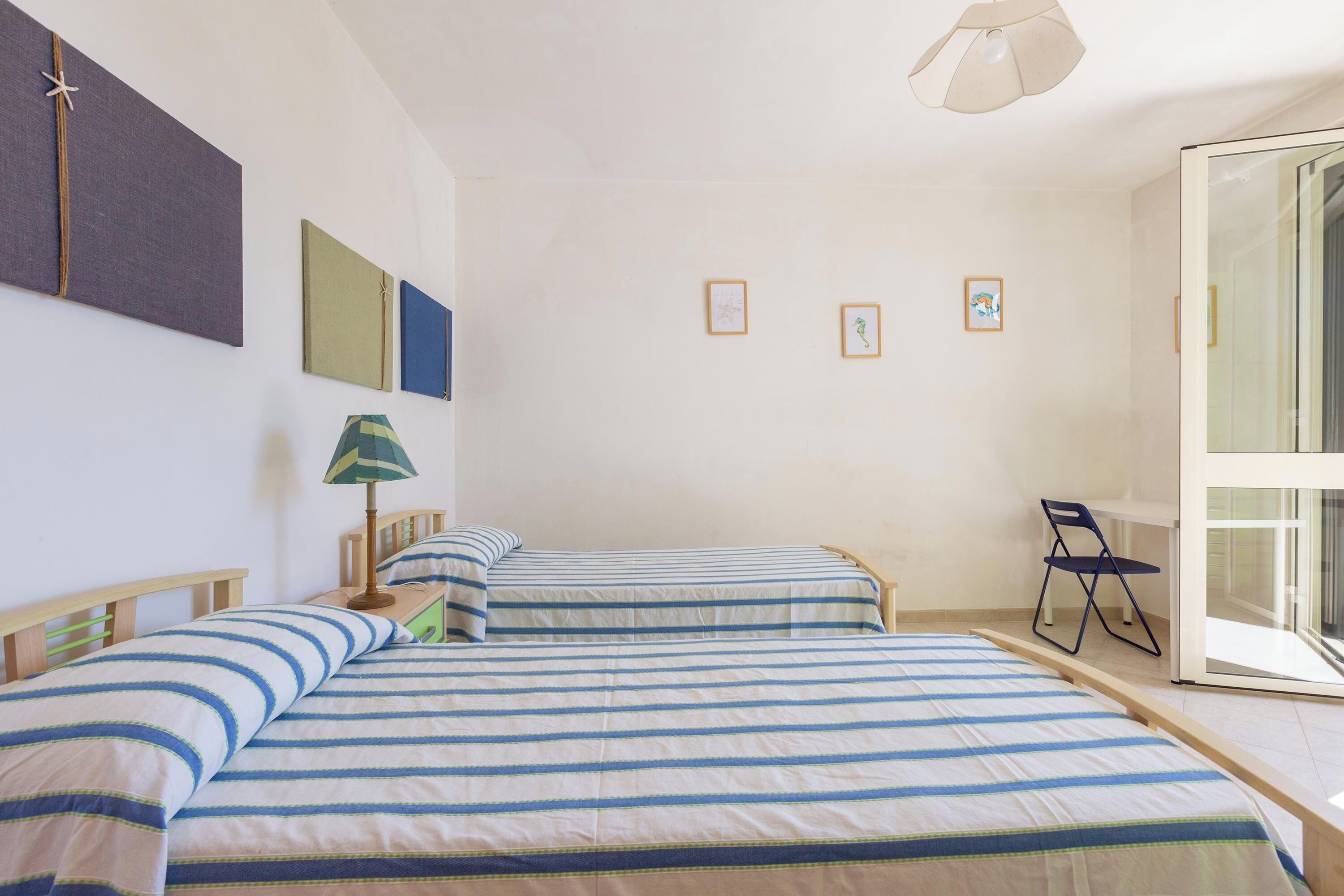 Ein Zimmer mit zwei Betten, einem Schreibtisch, einem Stuhl und einem großen Fenster.