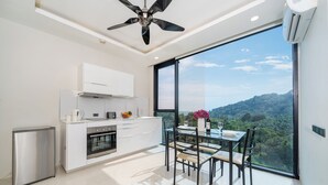 A modern kitchen with a dining area, large windows, and a view of a mountainous landscape. - Tropical View Suite A603 at Viva Patong (Patong)