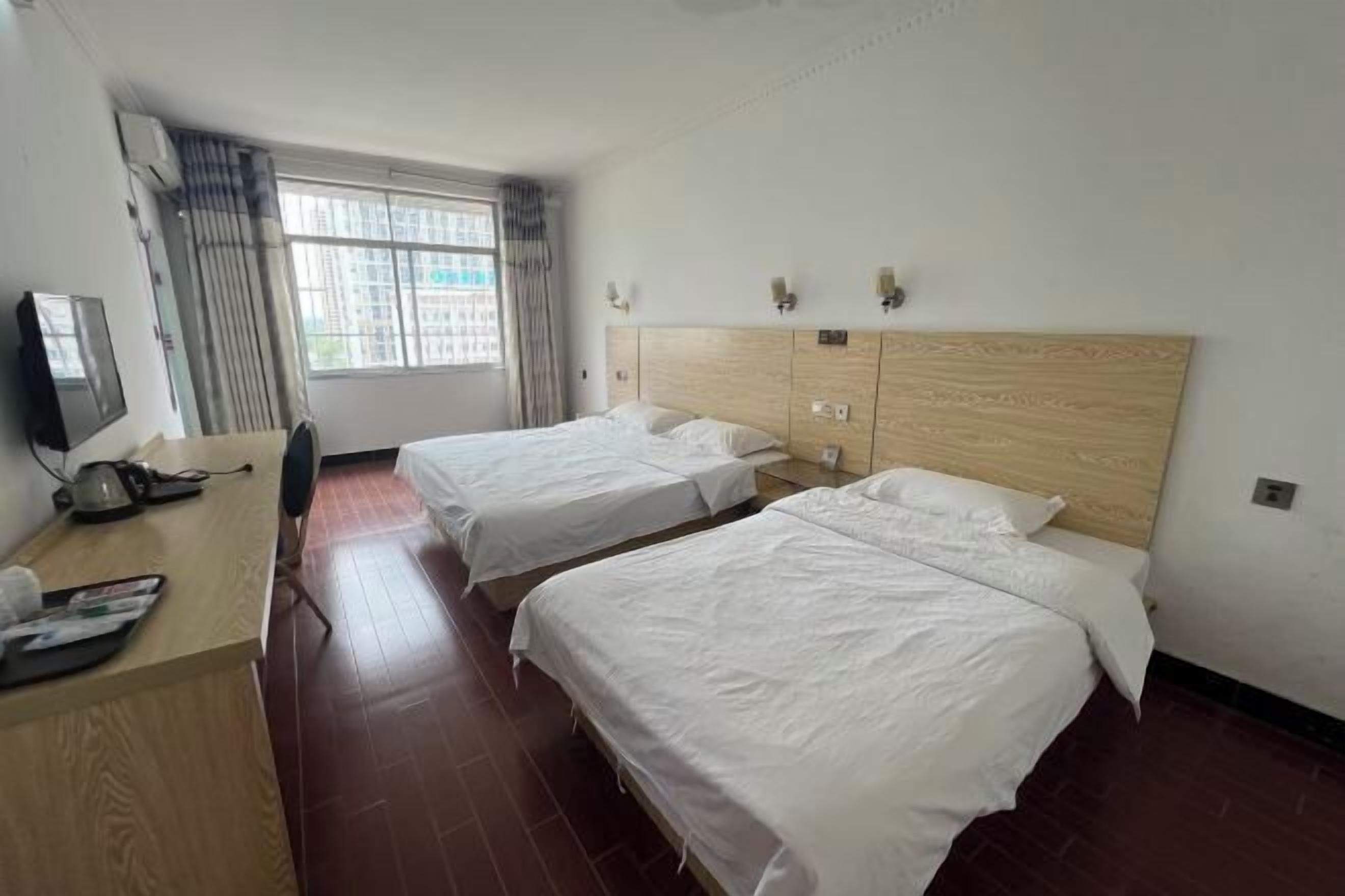 A hotel room with two single beds, a wooden desk with a chair, a TV, and a window with curtains.