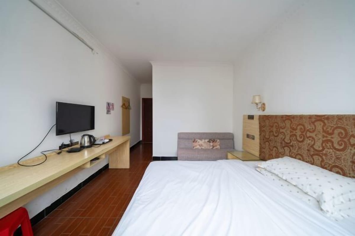 Een hotelkamer met een bed, een bureau met een televisie, een stoel en een klein tafeltje.