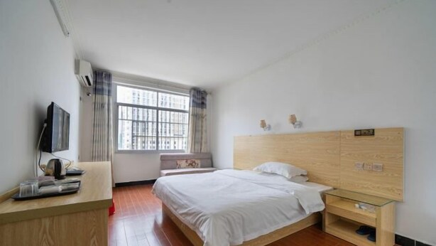 A bedroom with a wooden bed, a bedside table, a TV on a stand, and a window with curtains. - Nanning Boqian Business Hotel (Nanning)