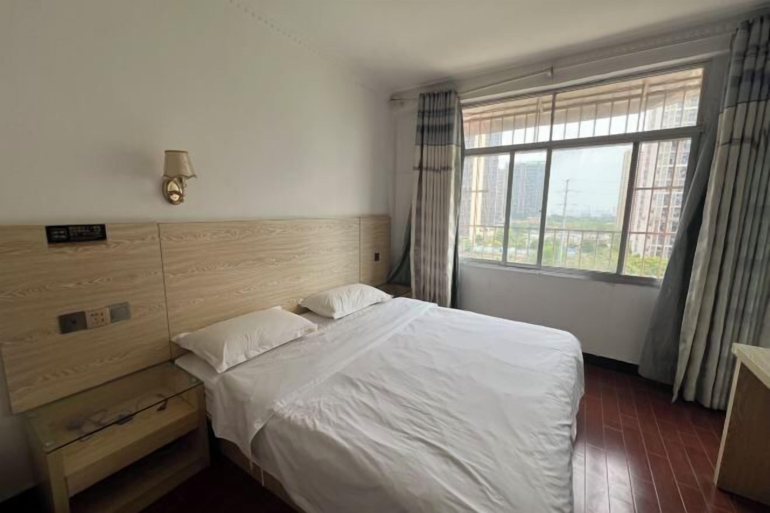 Habitación de hotel con una cama grande, una mesita de noche, una lámpara de pared y una ventana con cortinas.