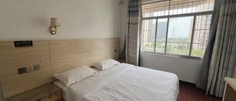 Habitación de hotel con una cama grande, una mesita de noche, una lámpara de pared y una ventana con cortinas.