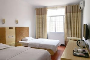 Een hotelkamer met twee eenpersoonsbedden, een houten hoofdbord, een tafeltje met een waterkoker, bekers en een dienblad, en een aan de muur bevestigde televisie.