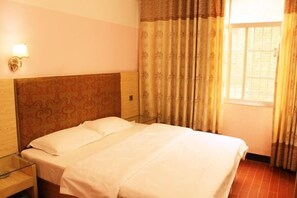 Een hotelkamer met een bed, nachtkastje, lamp en een raam met gordijnen.