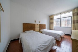 Een hotelkamer met twee enkele bedden, een houten hoofdeinde, een raam met gordijnen en een betegelde vloer.
