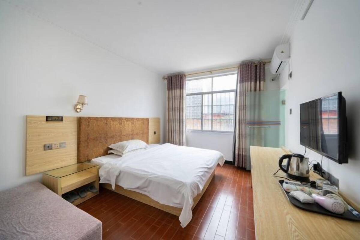 A hotel room with a wooden bed, a small bedside table, a TV, and a window with curtains.