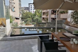 A balcony with a view of a cityscape, a pool, and outdoor furniture.