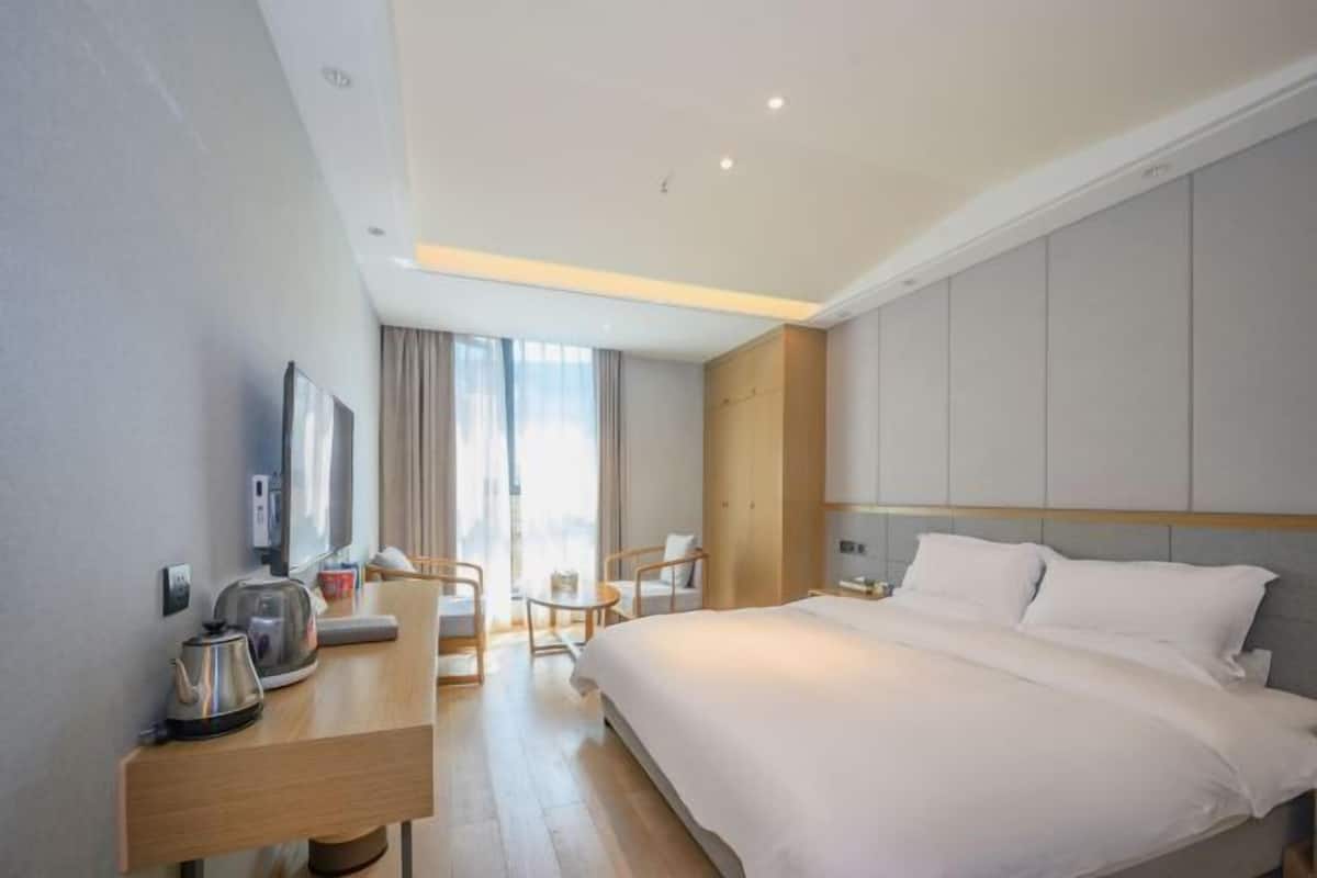Una habitación de hotel moderna con una cama grande, un escritorio con un hervidor, una silla y un televisor.