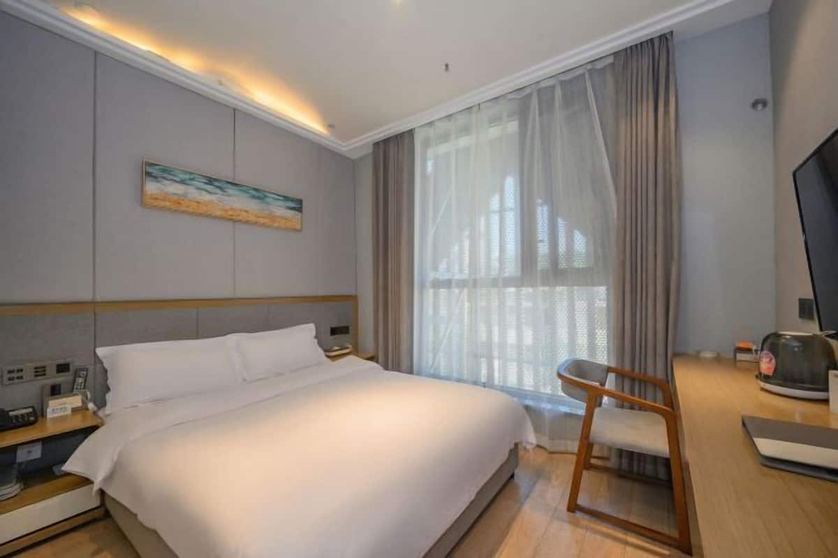 Habitación de hotel con cama, escritorio con silla, televisor y un cuadro en la pared.