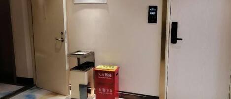 A hotel room with a door, a trash bin, and a red box on the floor.