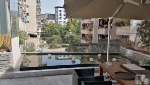 A rooftop terrace with a glass balustrade, a dining table with chairs, and a view of surrounding buildings and greenery.