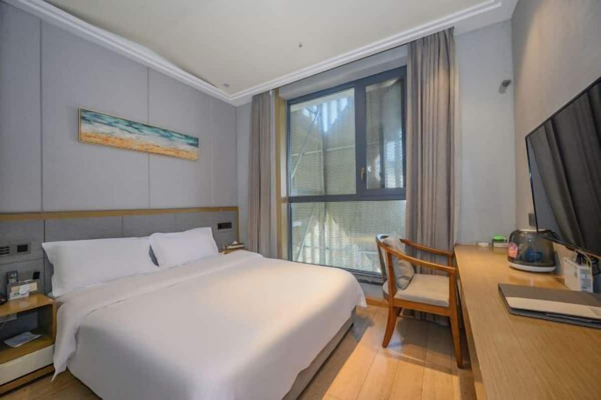Habitación de hotel con cama, escritorio, silla, ventana con cortinas y un cuadro en la pared.