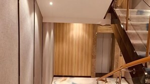 A modern interior with a wooden panel wall, a staircase with glass railings, and a neutral-toned floor.