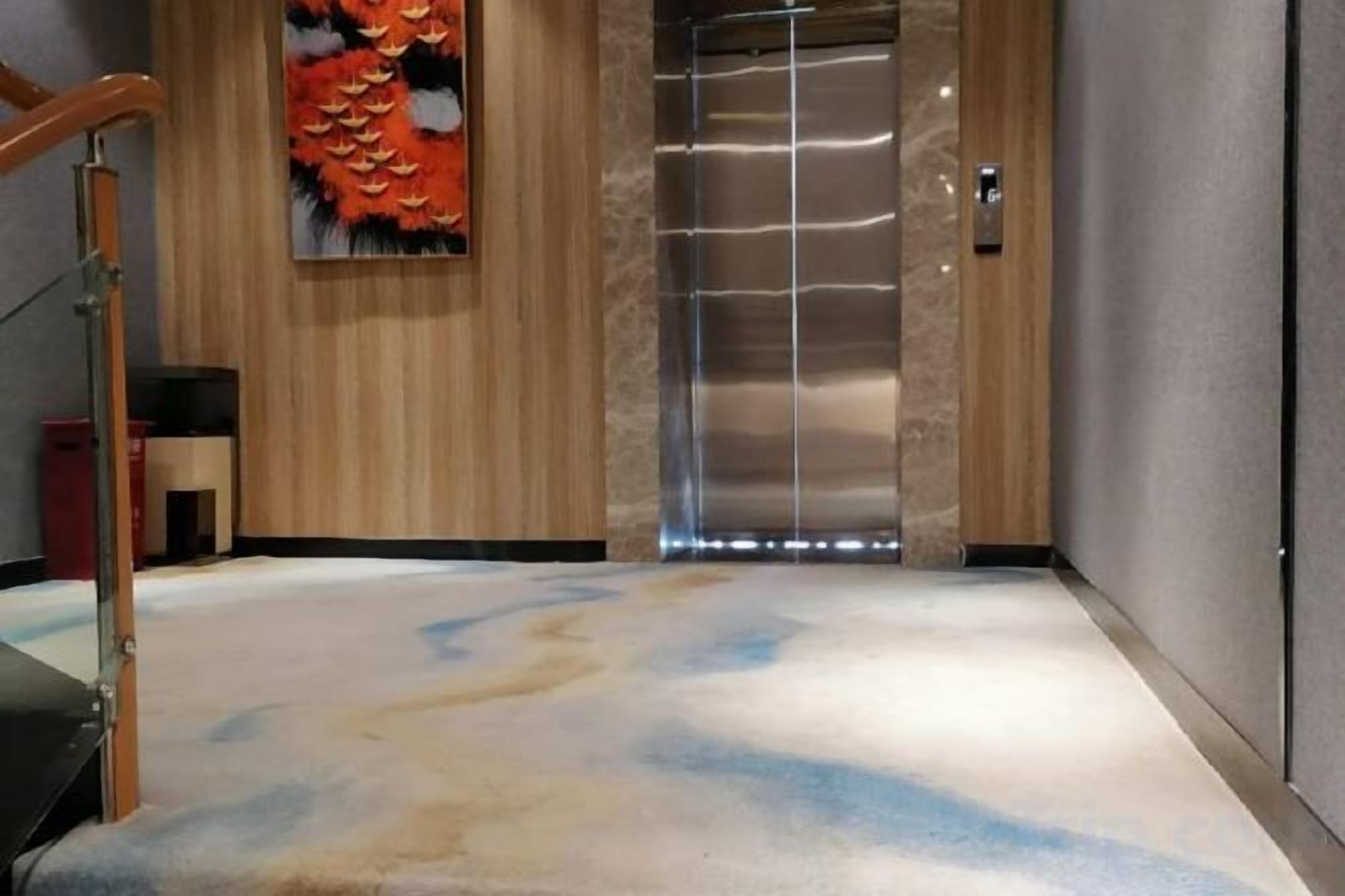 A hotel lobby with a wooden floor, a large artwork, and a modern elevator.