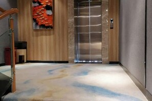 Un vestíbulo de hotel con piso de madera, una obra de arte grande y un ascensor moderno.