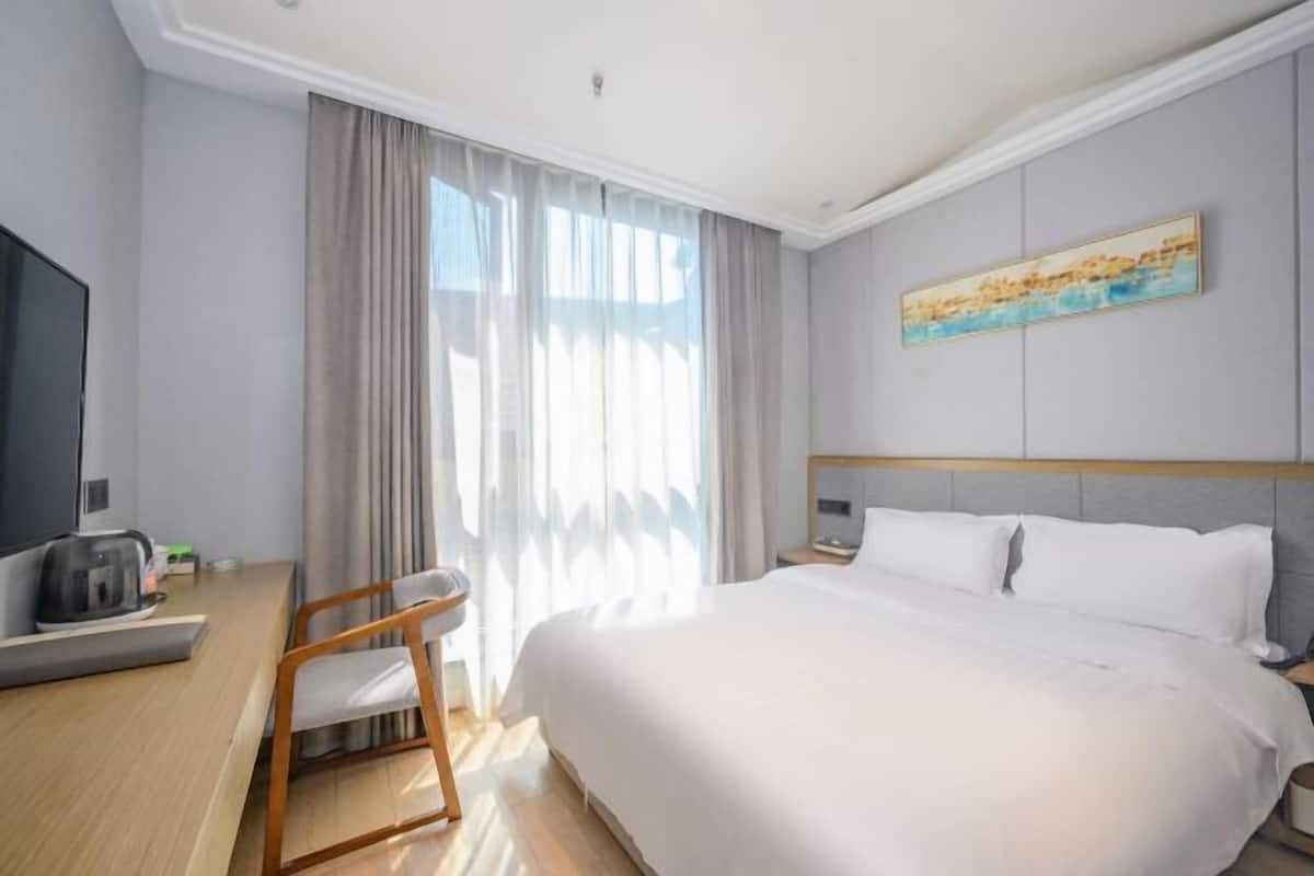 Una habitación de hotel con una cama, un escritorio con una silla, un televisor y un cuadro en la pared.
