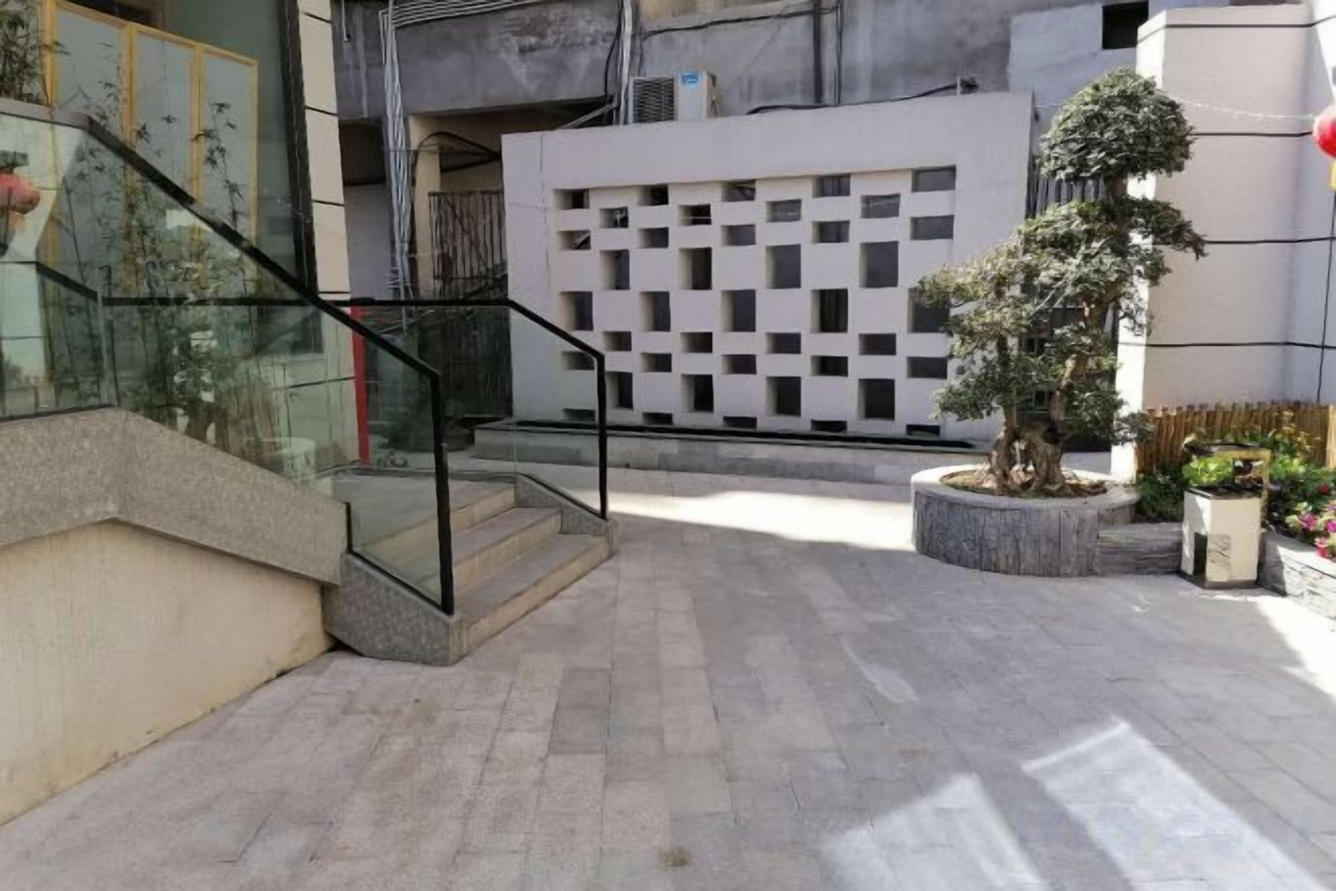 Une cour avec un escalier, un arbre en pot et la façade d’un immeuble moderne.