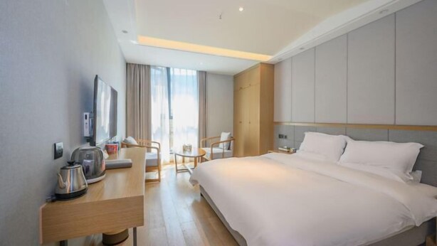 A modern hotel room with a large bed, a desk with a kettle, a chair, and a TV.