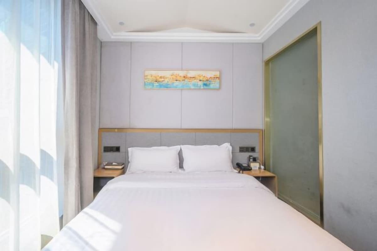 A hotel room with a bed, nightstands, a painting, and a door.