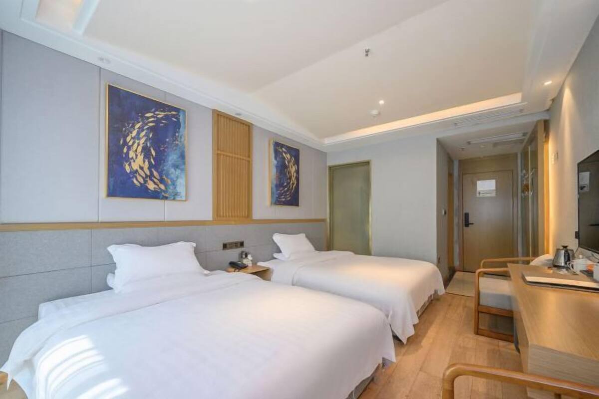 Habitación de hotel con dos camas, un escritorio y obras de arte en las paredes.