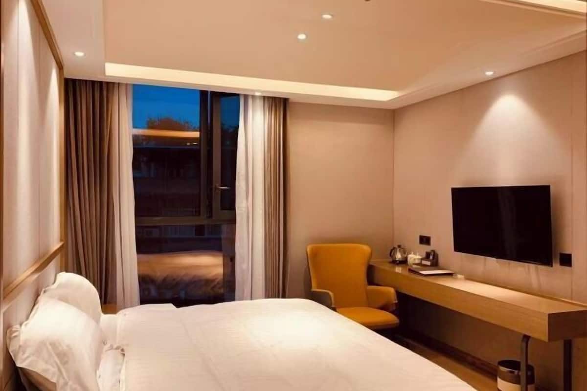 Habitación de hotel con cama, escritorio, silla, televisor y ventana con cortinas.