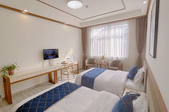 A hotel room with two beds, a desk with a chair, a TV, and a window with curtains.