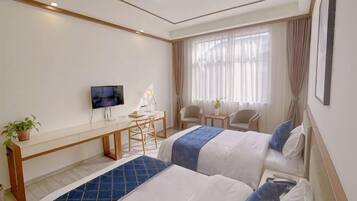 A hotel room with two beds, a desk with a chair, a TV, and a window with curtains.