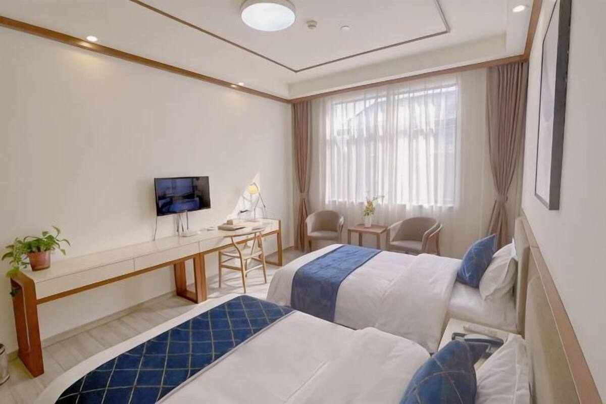 Een hotelkamer met twee bedden, een bureau, een televisie en een raam met gordijnen.