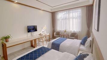 A hotel room with two beds, a desk, a TV, and a window with curtains.