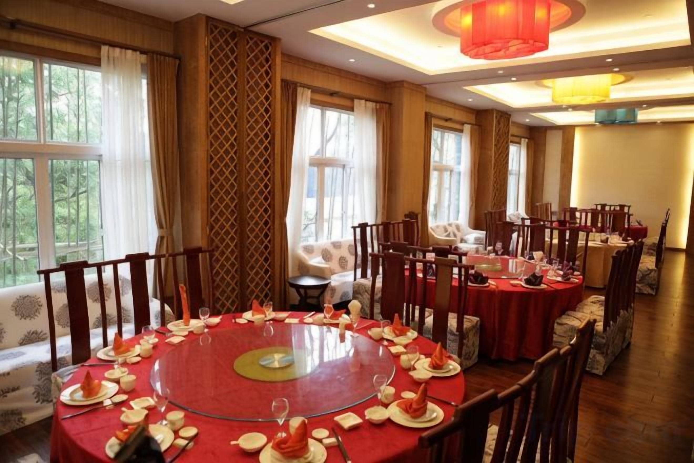 A round dining table with multiple chairs, a sofa, and a small table in a room with large windows and a patterned wall.