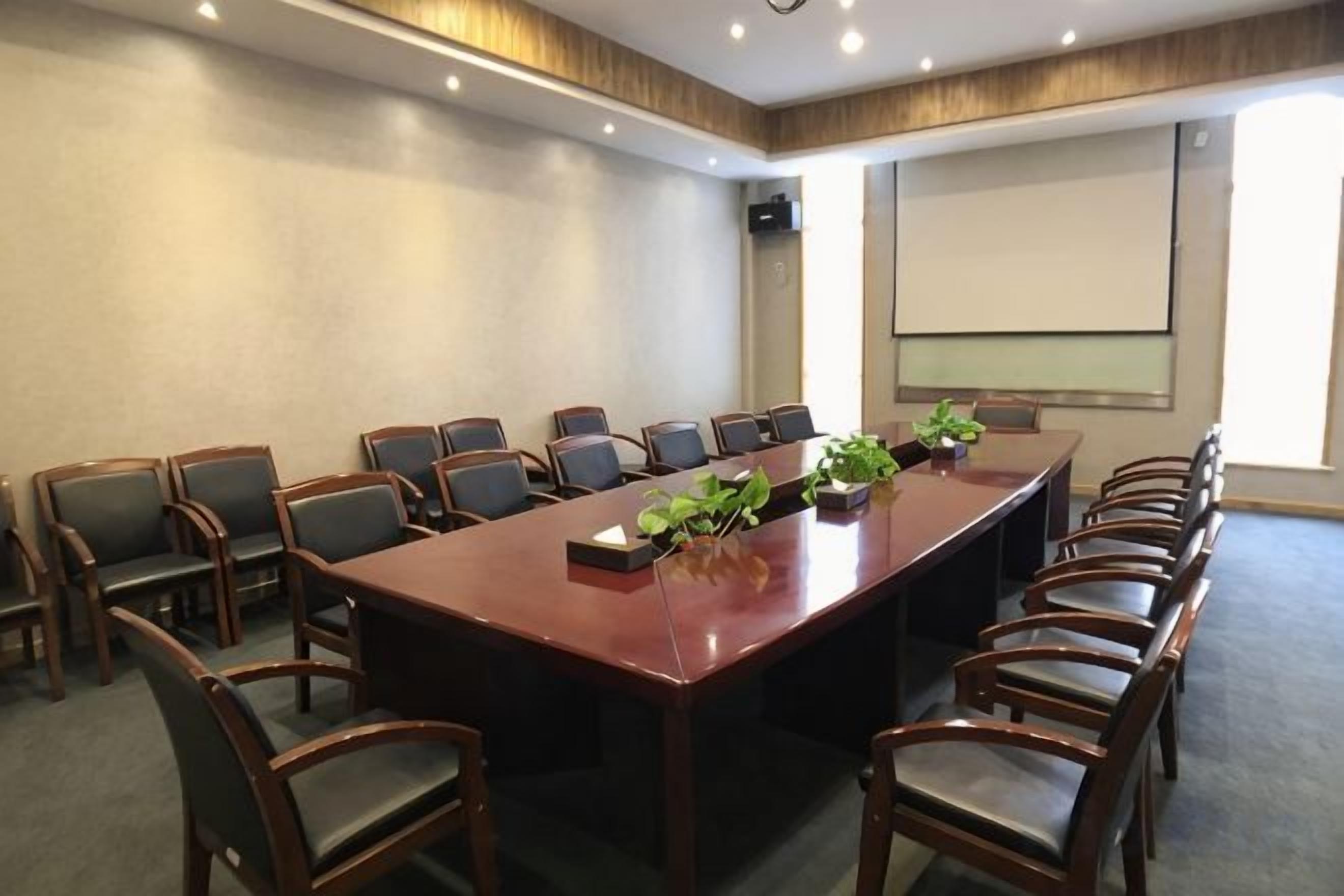 A conference room with a long table, multiple chairs, a projector screen, and a plant on the table.