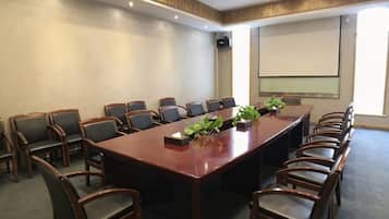 A conference room with a long table, multiple chairs, a projector screen, and a plant on the table.