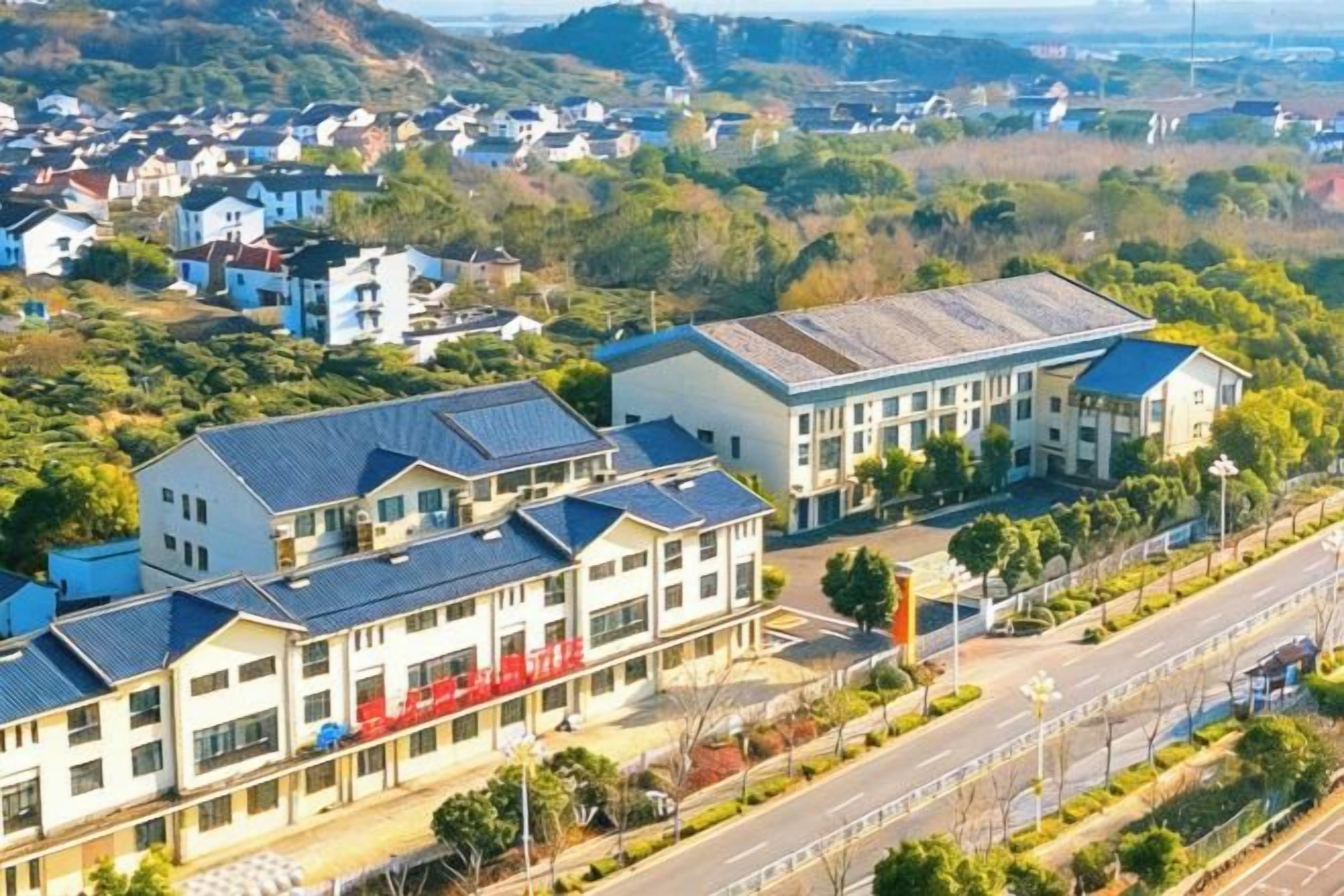 A residential area with modern buildings, a main road, and a hilly landscape in the background.
