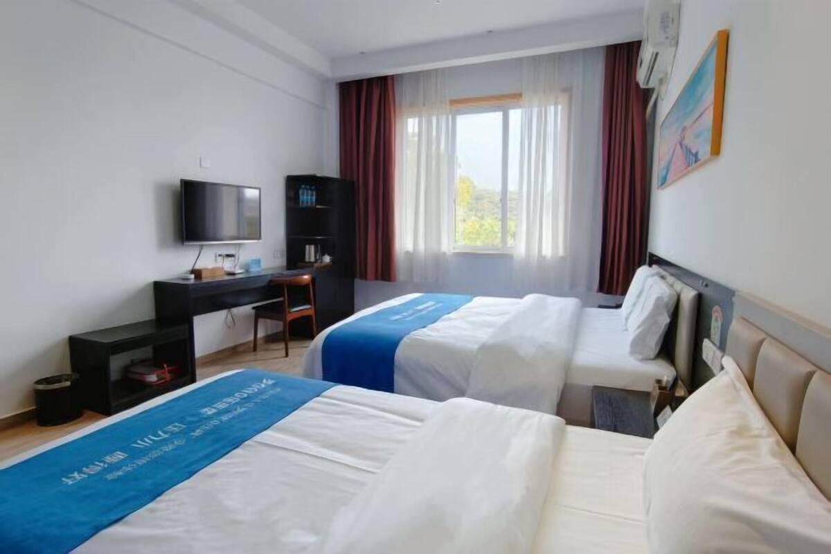 Een hotelkamer met twee bedden, een bureau, een televisie en een raam met gordijnen.