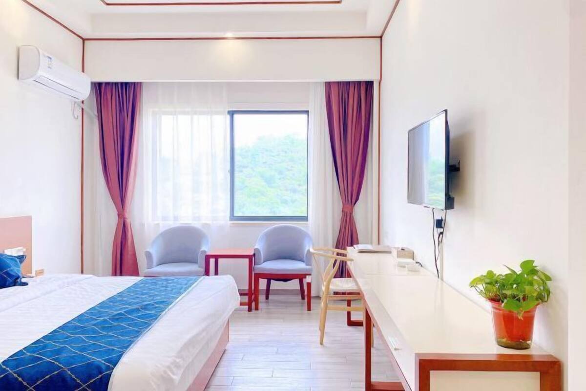 Een hotelkamer met een bed, twee stoelen, een bureau, een televisie en een raam met gordijnen.