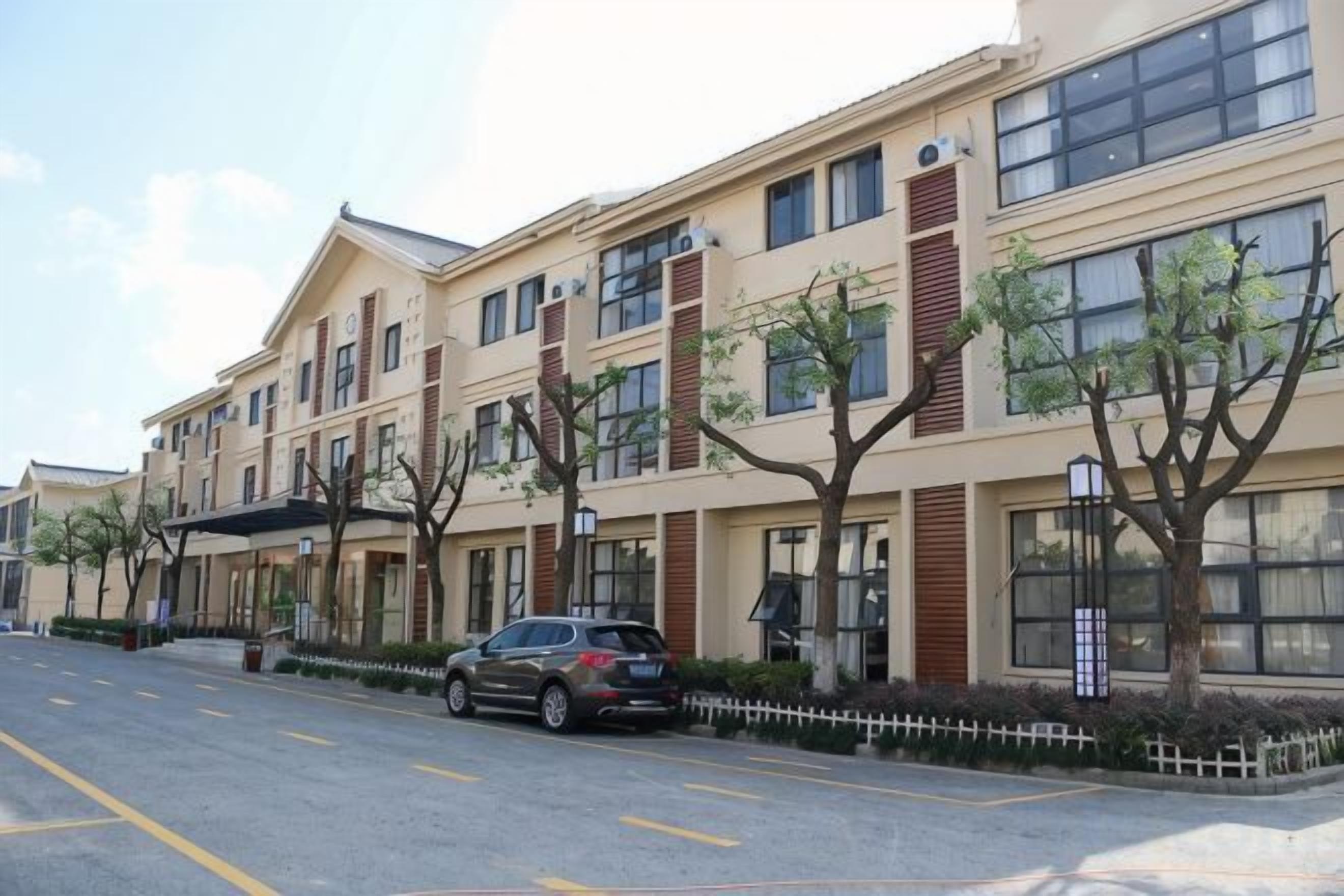 A multi-story building with a parking lot and trees along the street.