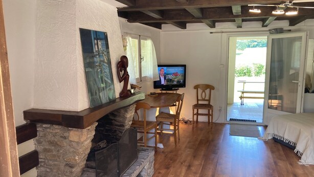 A cozy living room with a stone fireplace, wooden flooring, and a television displaying a news channel. - Quiet house in the Black Mountain (Les Martys)