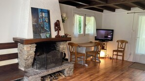 A cozy living room with a stone fireplace, wooden flooring, a television, and two wooden chairs. - Quiet house in the Black Mountain (Les Martys)
