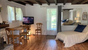 A cozy room with a wooden floor, a bed with a white cover, a television on a wooden table, and a window with curtains. - Quiet house in the Black Mountain (Les Martys)