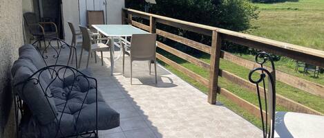 A patio with a sofa, chairs, and a table, overlooking a green landscape.