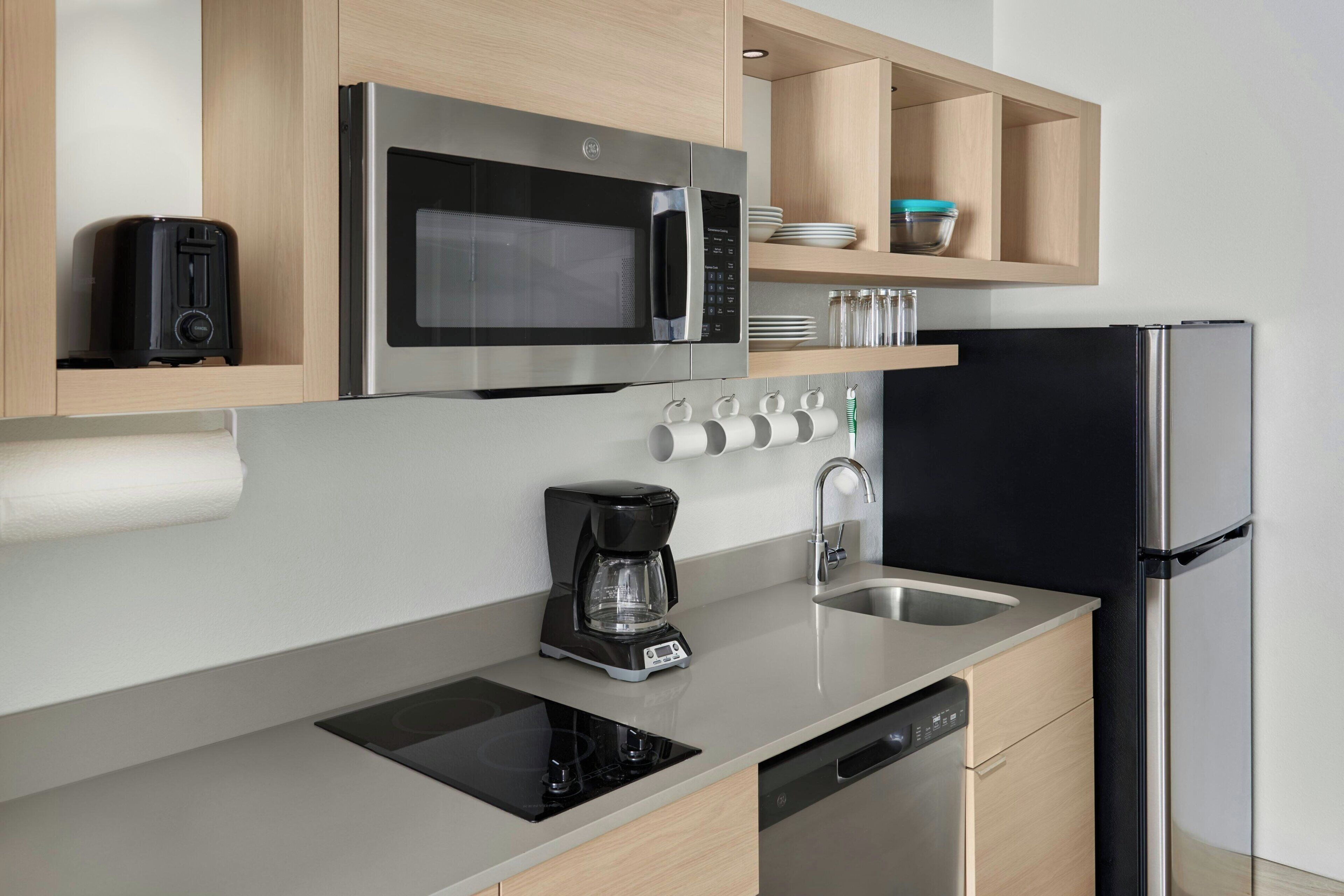 A modern kitchen with a built-in microwave, coffee maker, dishwasher, and a black refrigerator.