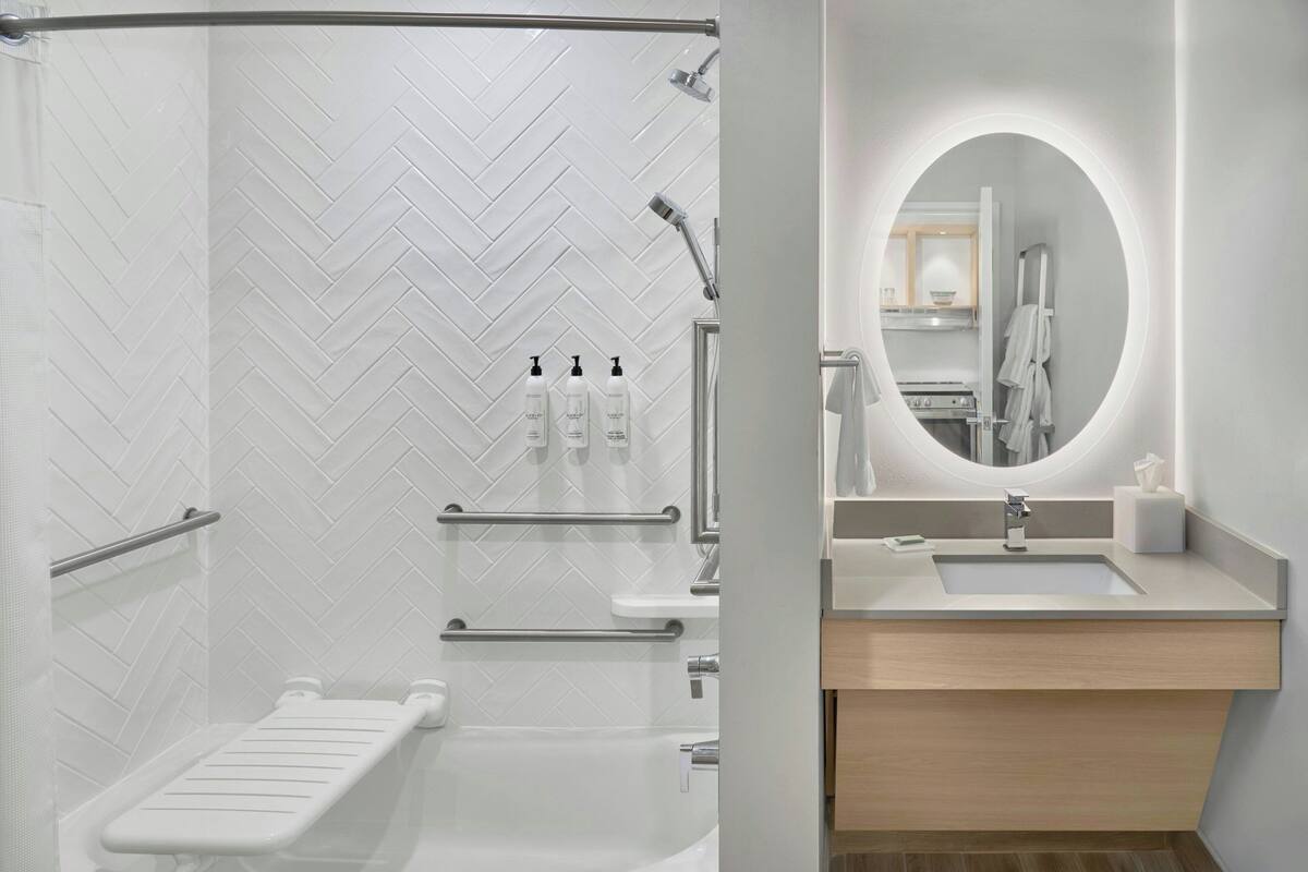 A modern bathroom with a herringbone tile backsplash, a shower with a glass door, a vanity with a mirror and sink, and a towel rack.