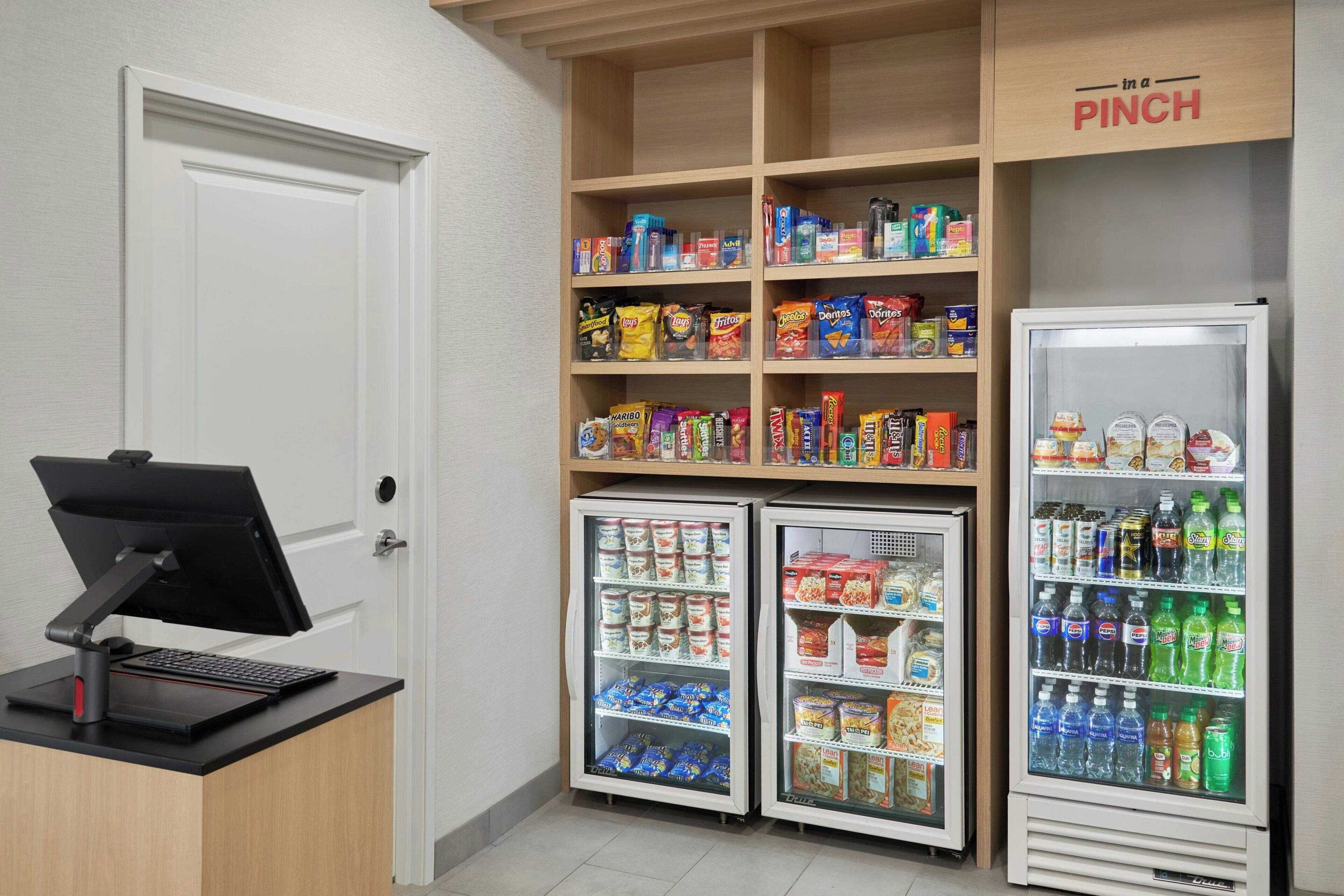 A small convenience store with a cash register, refrigerated freezers, and shelves stocked with snacks and beverages.