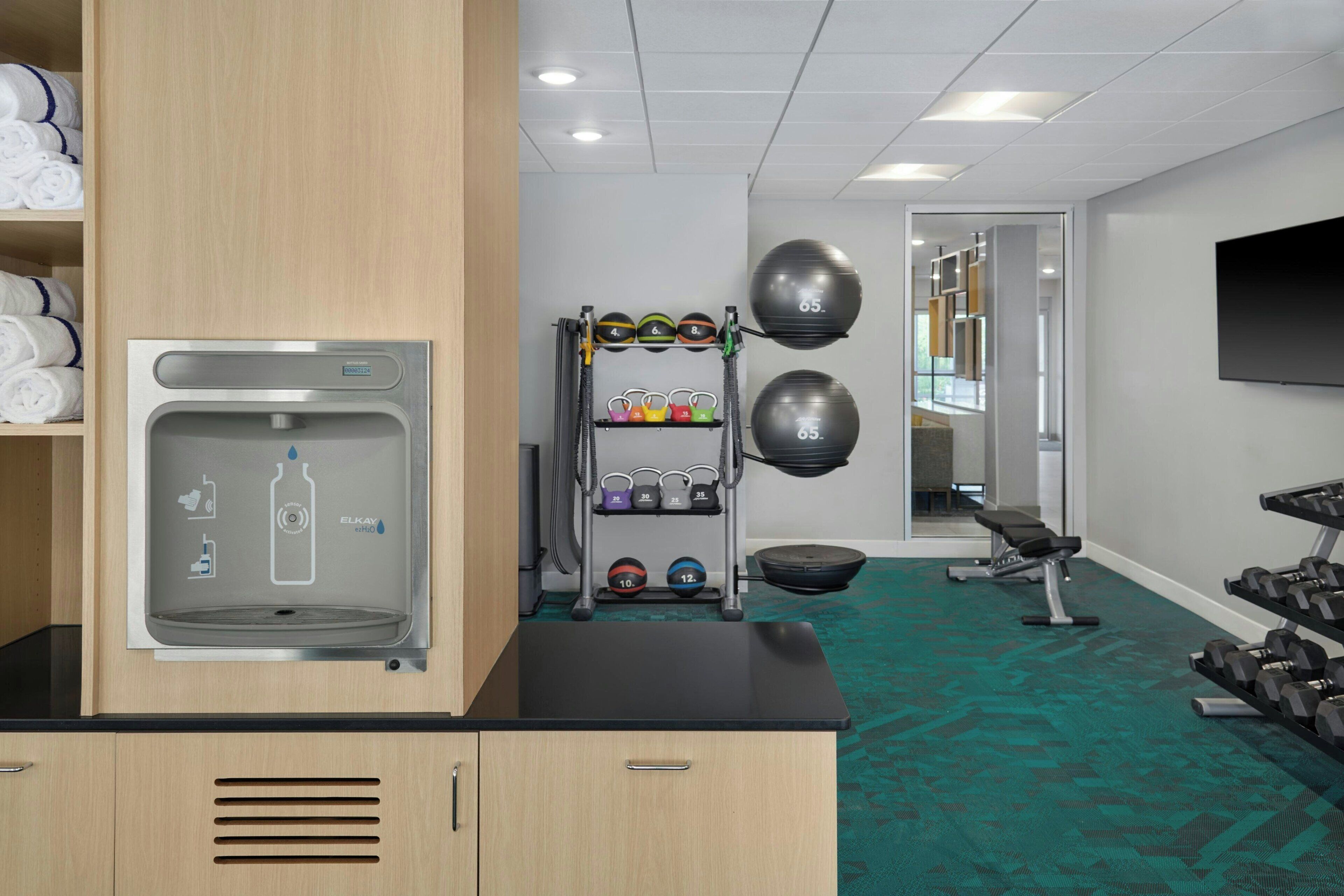 A gym with exercise equipment, a water dispenser, and neatly folded towels on shelves.
